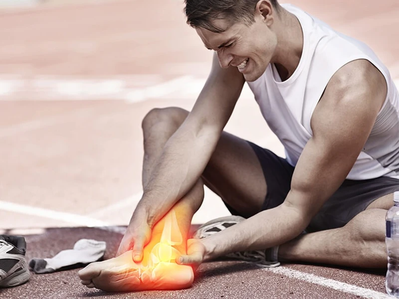 Koşu pistinde ayak bileğini tutan sporcu, ağrıyan bölge vurgulu